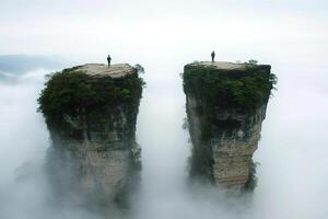 Two people stand on top of two rock formations in the clouds photo