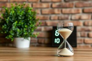 An hourglass sitting on a table with a clock photo