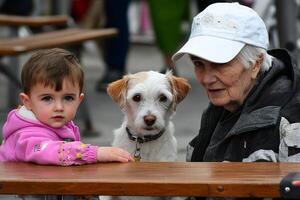 A little girl and an old lady sitting at a table with a dog photo