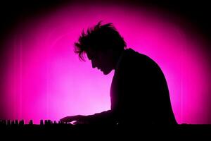 A man in a suit is playing a keyboard in front of a pink light photo