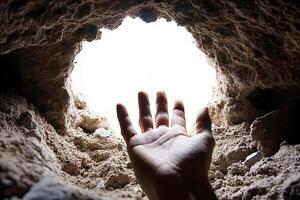 A person reaching out to the light from a cave photo