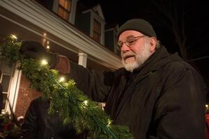 A man holding a christmas wreath in front of a house photo