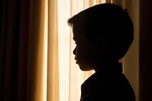 A silhouette of a boy standing in front of a window photo
