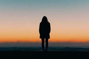 Silhouette of a woman standing on the beach at sunset photo