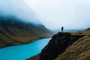 A person standing on a cliff overlooking a lake photo
