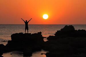 A person standing on a rock at sunset photo