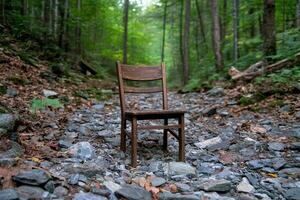 A chair sits on the side of a rocky path in the woods photo