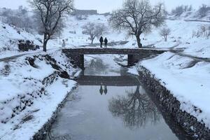 Two people walk across a bridge over a small stream photo