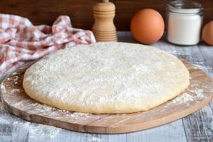 A pizza dough on a wooden board with eggs and flour photo