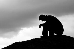 A man sitting on top of a mountain with a dark sky photo
