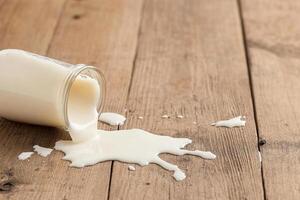 Milk pouring from a glass on a wooden table photo