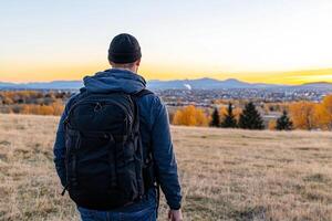 A man with a backpack standing in a field looking at the sunset photo