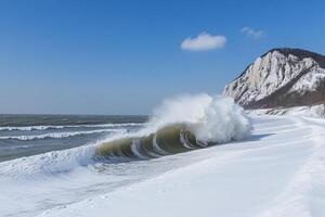 A large wave breaking on the beach in front of a cliff photo