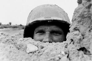 A man in a helmet peeking out from a hole in the sand photo