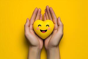 Hands holding a smiling heart on yellow background, expressing love, care, and happiness photo