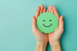 Hands holding a green circle with a happy smiley face on turquoise background photo