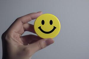 Hand holding yellow round button with smiley face, expressing happiness and positivity photo
