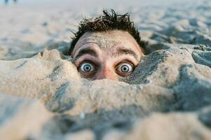 Man buried in sand showing only his head and eyes on the beach photo