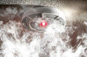 Smoke detector sensing smoke and flashing red alert light photo