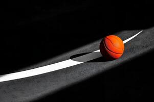 Basketball resting on court line in darkened gym with dramatic lighting photo
