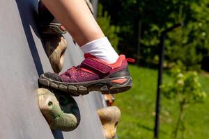 Child leg in sneaker bouldering on artificial rock wall ourdoor photo