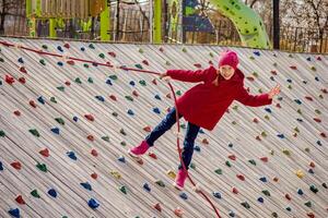 Happy child climbing on artificial rock wall using rope on playground photo