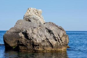 Large stone in calm blue sea water photo