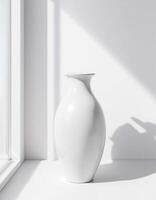 A white vase sitting on a white table near a window photo
