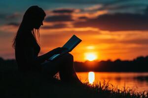 Silhouette of a person reading a book at sunset by the water. photo