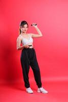 A woman wearing a white top, black pants, and white sneakers, holding a skipping rope, posing for a picture isolated on a red background photo