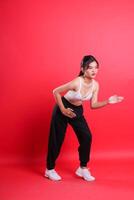 A woman in a white sports bra and black pants, with white sneakers is seen posing with arms extended. isolated on a red background photo