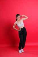 A woman wearing a white sports top and black pants flexing her bicep, standing against a red background. isolated on a red background photo