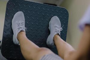 close up showing a woman's legs on a leg press machine. Both feet are positioned in the middle of a metal platform. wearing white shoes with laces and a short skirt photo