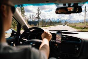 Tourist driving car and using smartphone for navigation while traveling on sunny day towards High Tatras mountain range in Poland. Driver navigating via smartphone while traveling sunny roadway photo