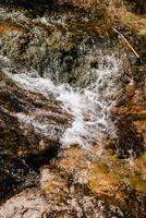 Crystal clear water flows over moss covered rocks, creating mesmerizing cascade in pristine natural setting, showcasing beauty and tranquility of untouched wilderness. Water cascading over moss rocks photo