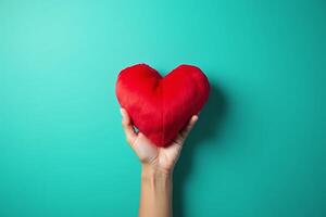 A single hand holding a red heart shaped pillow on a turquoise background with copy space for message. photo