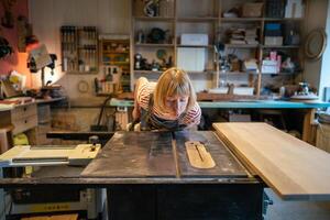 Female handywoman blowing dust off table surface before starting circular saw work in workshop photo