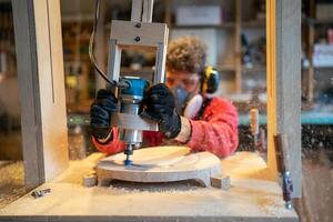 Joiner shaping stool base on drilling cnc machine in workshop. Furniture smoothing, production photo