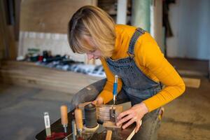 Pedant woman joiner works in joinery workshop, sanding, turning wooden knife blanks on lathe photo