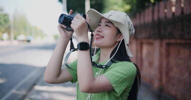 Handheld selective focus shot, Happy young Asian woman standing enjoying the surrounding view while taking photo with her camera. video