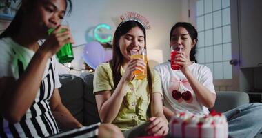 Three friends are celebrating a birthday party, smiling and clinking their colorful drinks together in a joyful moment. Share special moments together at home video