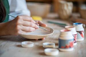Ceramic plates painted by craftswoman hands, adding unique patterns on wooden table. Paint design photo