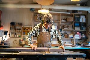 Carpentry workshop, craftsman master working. Man uses circular woodworking machine. photo