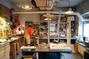 Rearview of busy carpenter preparing tools for woodworking in workshop, setting up machinery photo