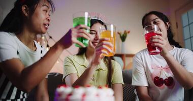 Handheld low angle view shot, Three friends are celebrating a birthday party, smiling and clinking their colorful drinks together in a joyful moment. Share special moments together video