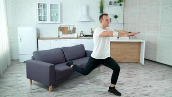 Young man exercising at home. Guy doing squats with a leg on sofa in the kitchen during isolation at pandemic. Sports training in apartment. video