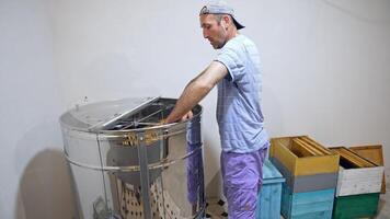 Honey production. Professional apiarist taking out frames from centrifuge machine indoors. Beekeeping process for harvesting natural honey on a farm. video
