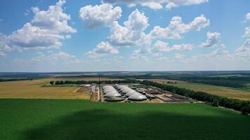Enterprise surrounded by fields. Biogas plant among nature in bright summer day. Large storage reservoirs for biogas production. Aerial view. video