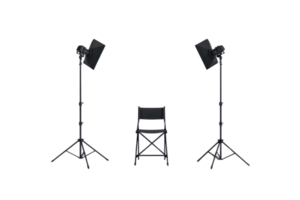 A simple black chair is flanked by two lighting stands, creating a setup for an interview or photo shoot. png