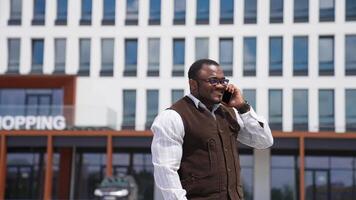 Portrait of happy african american man in city. Smiling black man in stylish glasses talking the phone while standing outdoors. Businessman with a phone looks at camera. video